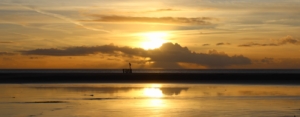 Sonnenuntergang am Meer, im Vordergrund aufgelaufenes Wasser, dahinter Strand, am Horizont das Meer, darüber Himmel mit Wolken, und alles in goldenes Licht getaucht (Foto: Birte Vogel)