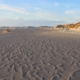 Im Vordergrund wellenförmige Strukturen im Sand, die vom Standpunkt aus in die Bildmitte hochlaufen; rechts einige Dünen, links Wasser, darüber blauer Himmel mit einigen Wolken (Foto: Birte Vogel)