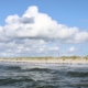 Im Vordergrund Meereswellen, dahinter ein Strand mit einigen bunten Strandkörben, dahinter ein breiter Dünengürtel. Darüber ein blauer Himmel mit einigen weißen und grauen Wolken. (Foto: Birte Vogel)